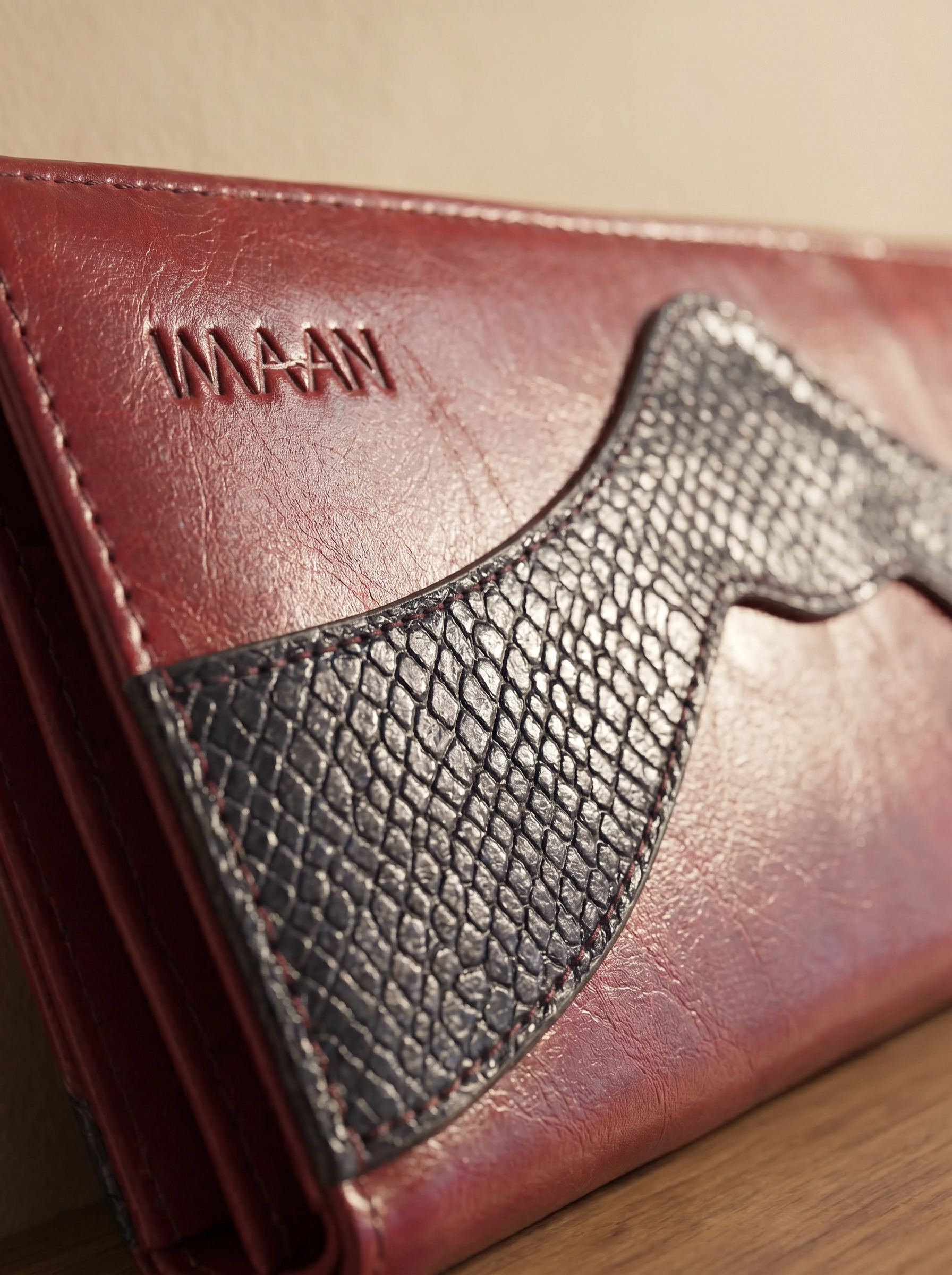 Close-up of a brown leather wallet with 'IMAAN' branding on a wooden surface.